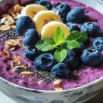 Blueberry spinach smoothie bowl topped with fresh fruit and seeds.